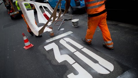 Ein Arbeiter bringt eine Tempo-30-Markierung auf einer Straße an