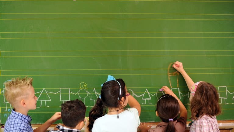 kinder stehen an einer Schultafel - in Ludwigshafen an einer Grundschule werden voraussichtlich 40 Kinder die erste Klasse nicht schaffen. (Foto: dpa Bildfunk, Jonas Güttler)