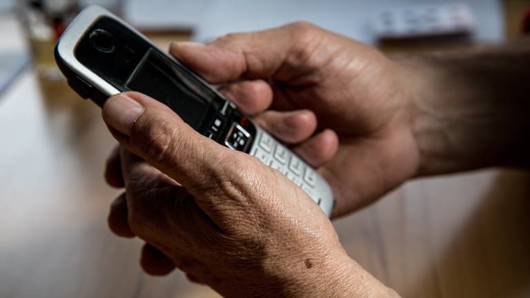 Die Hand eines älteren Menschen hält ein Telefon in der Hand.  (Foto: picture-alliance / Reportdienste, picture alliance / Fotostand | Fotostand / K. Schmitt)