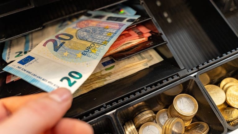 Eine Hand zieht einen 20-Euro-Schein aus einer Geldkasse voll mit Bargeld. Symbolbild für graue Kassen, die in Neustadt an der Weinstraße abgeschafft werden