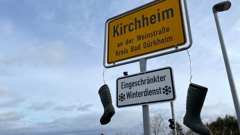 Bauernprotest in der Pfalz. Landwirtschaftliche Stiefel über dem Ortsschild von Kirchheim an der Weinstraße