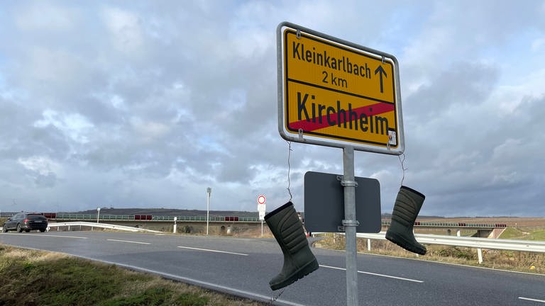 Bauernprotest in der Pfalz. Landwirtschaftliche Stiefel über dem Ortsschild von Kirchheim an der Weinstraße (Foto: SWR)