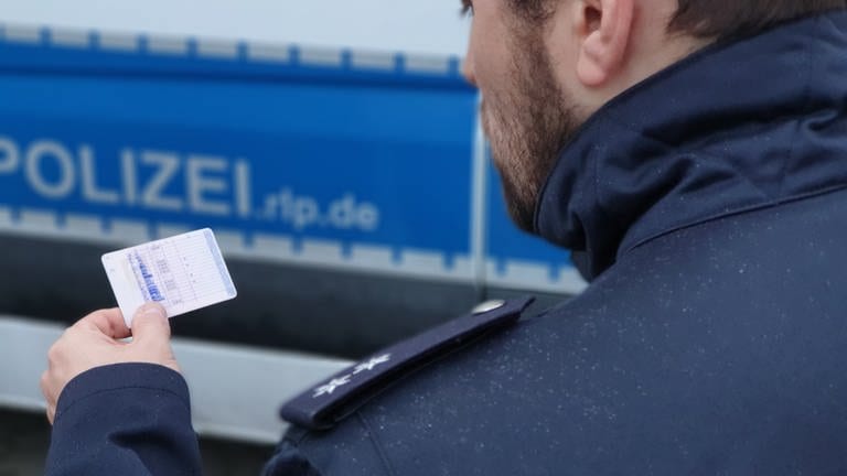 Polizist kontrolliert einen Führerschein - Symbolbild zur Meldung falsche Lkw-Fahrerin bei Dannstadt-Schauernheim erwischt