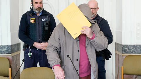 Mann steht vor Gericht und verbirgt sein Gesicht