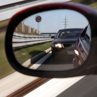 Ein Autofahrer sieht einen Drängler im Seitenspiegel, der viel zu dicht auffährt.  (Foto: dpa Bildfunk, Picture Alliance)