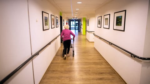 Eine ältere Frau läuft auf einem Flur in einem Altenheim mit ihrem Rollator spazieren (Foto: picture-alliance / Reportdienste, picture alliance/dpa | Federico Gambarini)