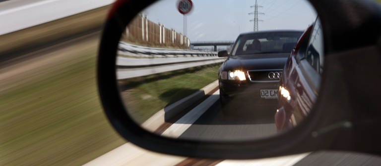Ein Autofahrer sieht einen Drängler im Seitenspiegel, der viel zu dicht auffährt.  (Foto: dpa Bildfunk, picture alliance/dpa | Marcus Führer)