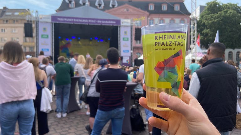 Ein Becher mit dem Logo des Rheinland-Pfalz-Tages 2022 wird am Schillerplatz vor der großen Landesbühne in die Luft gehalten. (Foto: SWR, Katharina Feißt)