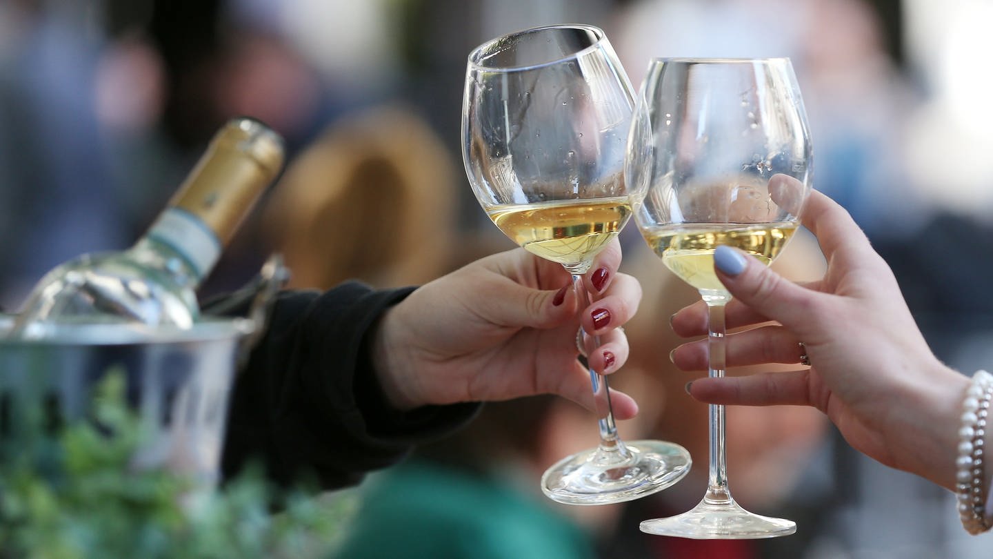 Frauen stoßen an einem Tisch im Außenbereich eines Lokals mit Weißwein an. In Rheinhessen eröffnen nach dem Corona-Lockdown wieder die ersten Weinstände.