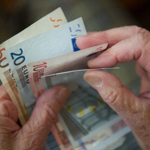 Eine ältere Frau hält mehrere Geldscheine in der Hand.