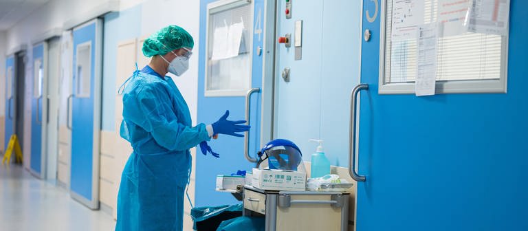 Eine Krankenhausmitarbeiterin in Corona-Schutzkleidung steht alleine in einem Krankenhausflur. (Foto: picture-alliance / Reportdienste, Picture Alliance)