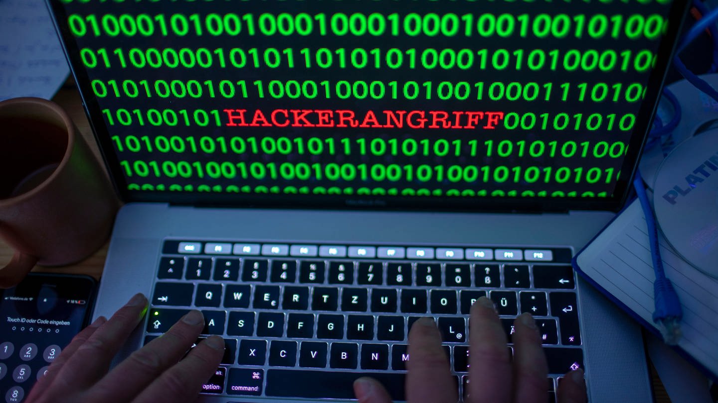 Zwischen dem Binärcode auf einem Laptopmonitor ist das Wort Hackerangriff zu sehen.