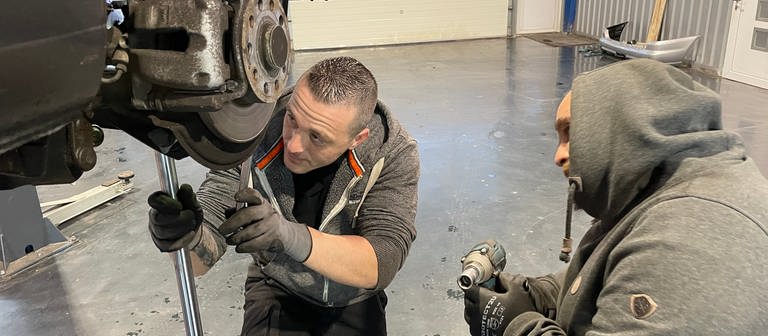 Zwei Männer schrauben an einem Auto. Manuel Saba betreibt in Gau-Algesheim eine Hobby-Werkstatt, wo Menschen ihr Auto selbst reparieren können. (Foto: SWR, Alexander Dietz)