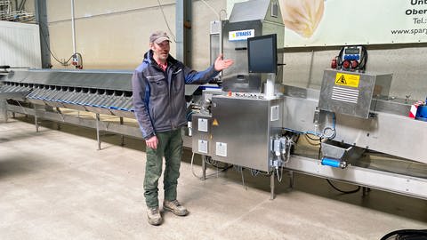 Landwirt Torsten Simmet aus Ober-Flörsheim steht kurz vor Beginn der Spargelernte in Rheinhessen vor einer Spargelsortiermaschine, die in einer Halle steht.  (Foto: SWR, S. Steinbrecher)