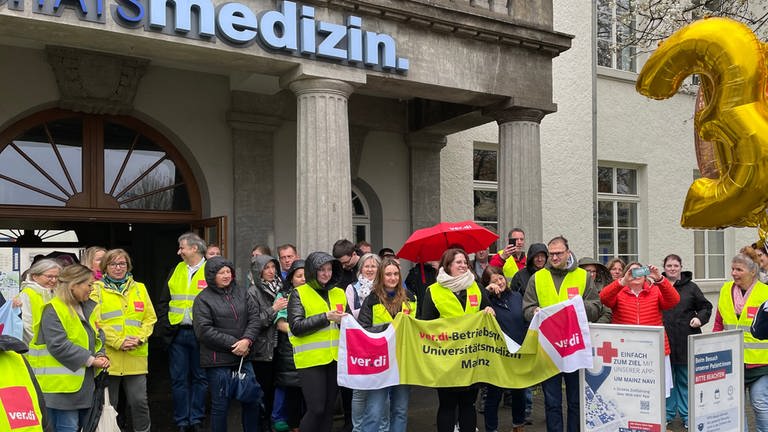 Nicht-ärztliches Personal der Mainzer Unimedizin steht mit Plakaten vor dem Eingang des Krankenhauses (Foto: SWR)