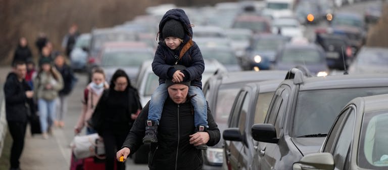 Ukrainische Flüchtlinge gehen mit ihrem Gepäck an Fahrzeugen entlang, die am Grenzübergang stehen. (Foto: dpa Bildfunk, Picture Alliance)