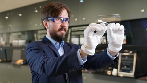 Ein Mitarbeiter von Schott führt vor, wie stark sich das ultradünne Glas von Schott biegen lässt. (Foto: Pressestelle Schott AG)