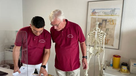 zwei Mediziner beugen sich in der Praxis über Patienten-Unterlagen (Foto: SWR)
