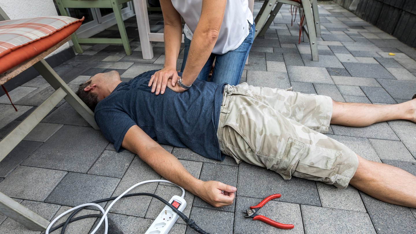 Ein Mann liegt bewusstlos am Boden und wird mit Herz-Druck-Massage reanimiert. (Foto: picture-alliance / Reportdienste, picture alliance / Jochen Tack | Jochen Tack)