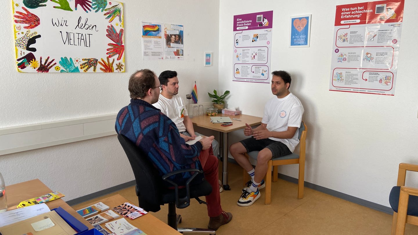 Zwei queere Männer sitzen bei Konsti Hahn in der Beratungsstelle für Flüchtlinge der Caritas in Mainz. (Foto: SWR)