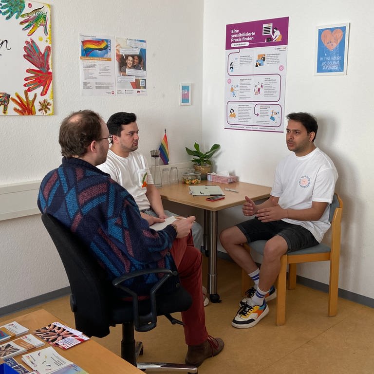 Zwei queere Männer sitzen bei Konsti Hahn in der Beratungsstelle für Flüchtlinge der Caritas in Mainz. (Foto: SWR)