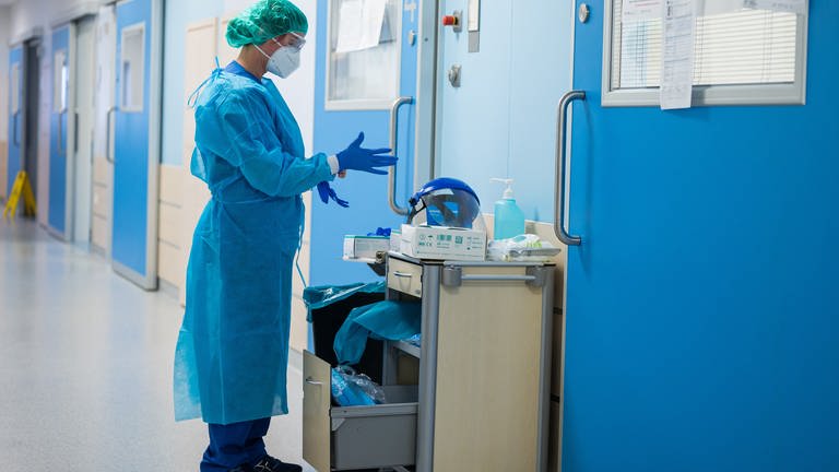 Eine Krankenhausmitarbeiterin in Corona-Schutzkleidung steht alleine in einem Krankenhausflur.