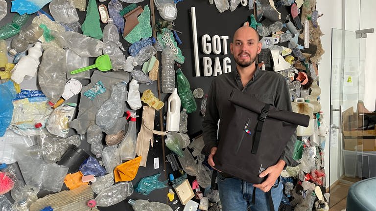 Got Bag-Gründer Benjamin Mandos steht mit einem Rucksack vor einer mit Plastik beklebten Wand (Foto: SWR)