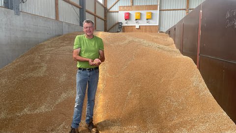 Adolf dahlem steht vor einem großen Haufen Getreidekörner in einer Halle (Foto: SWR)