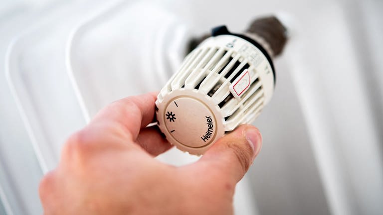 Ein Mann dreht in einer Wohnung am Thermostat einer Heizung. Die Wohnbau Mainz will die Temperaturen im Winter verringern, um Energie zu sparen.