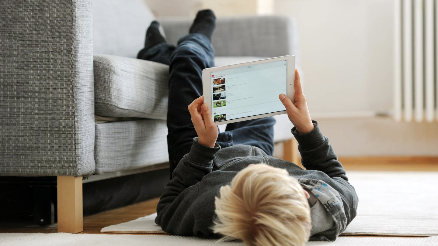Ein Jugendlicher liegt auf dem Fußboden und betrachtet die Video-Plattform Youtube auf seinem iPad. (Foto: dpa Bildfunk, Tobias Hase)