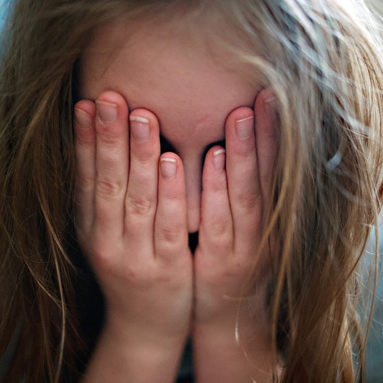 Ein junges Mädchen hält sich die Hände vor ihr Gesicht. 