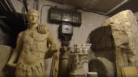Eine römische Skulptur sowie verzierte Pfeiler stehen im Keller unter einem Sicherungskasten. (Foto: SWR)