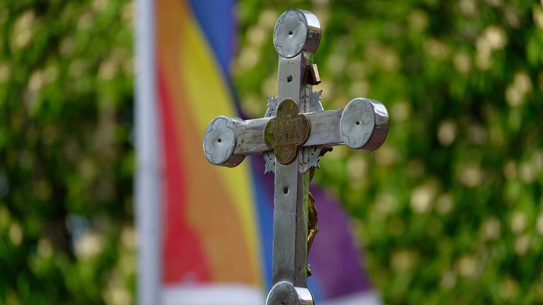 Ein Kreuz steht vor einer Regenbogenflagge. Im Bistum Mainz wird am Sonntag ein Gottesdienst zur Beauftragung der queersensibler Pastoral gefeiert. (Foto: dpa Bildfunk, picture alliance/dpa | Henning Kaiser)