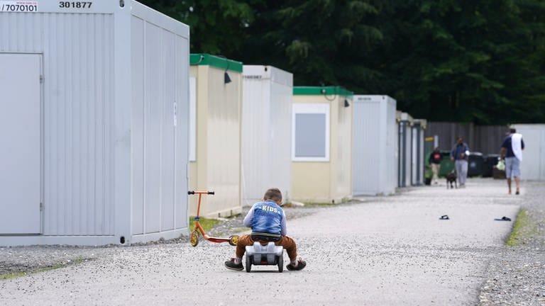 Eine Junge fährt auf einem Bobbycar vor den Wohn-Containern seiner Flüchtlingsutnerkunft. (Symbol) 