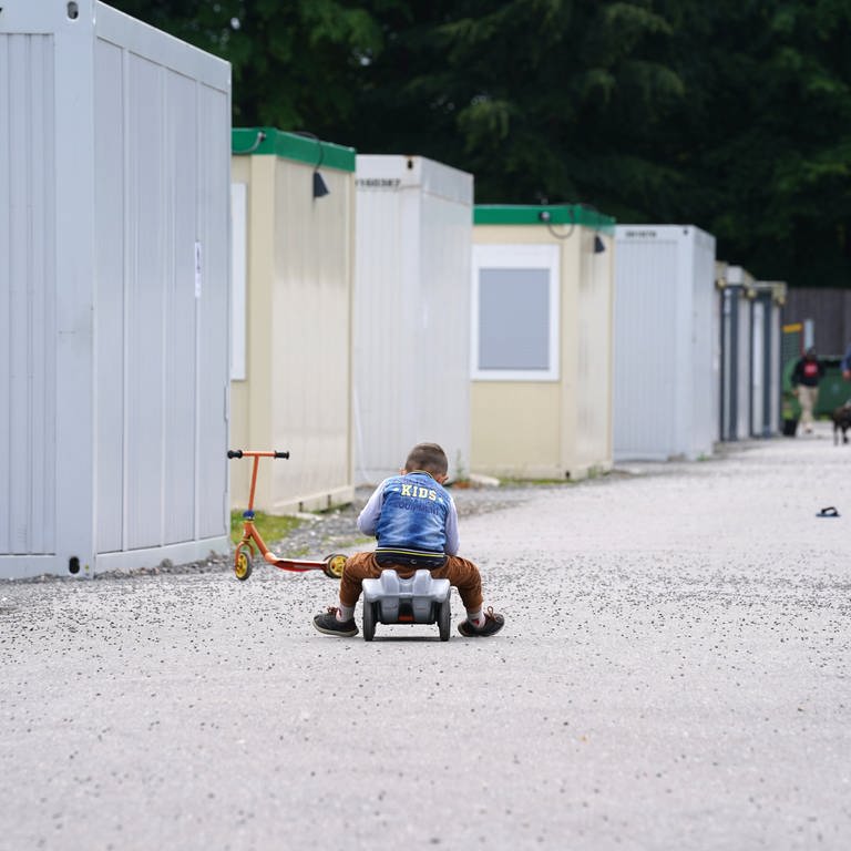 Eine Junge fährt auf einem Bobbycar vor den Wohn-Containern seiner Flüchtlingsutnerkunft. (Symbol)  (Foto: dpa Bildfunk, picture alliance/dpa | Marcus Brandt)