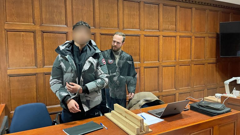 Der Angeklagte im Geldautomaten-Sprenger-Prozess wird am Mainzer Landgericht von seinem Anwalt an seinen Platz begleitet. Der 22-Jährige trägt Handschellen.