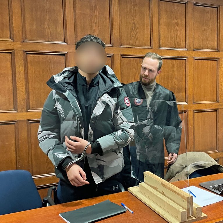 Der Angeklagte im Geldautomaten-Sprenger-Prozess wird am Mainzer Landgericht von seinem Anwalt an seinen Platz begleitet. Der 22-Jährige trägt Handschellen. (Foto: SWR, A. Dietz)