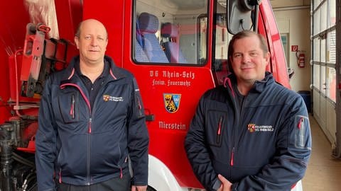 In der Feuerwache der VG Rhein-Selz stehen WehrleiterThomas Schäfer und Bürgermeister Martin Groth vor einem Feuerwehrfahrzeug. (Foto: SWR)
