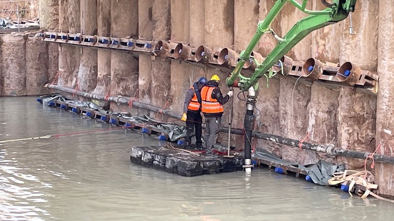 Ein Floß mit zwei Arbeitern in einer mit Wasser vollgelaufenen Baugrube