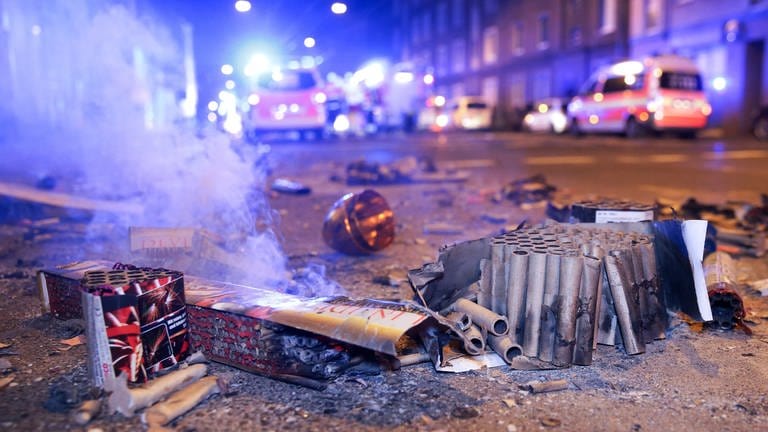 Eine abgebrannte Batterie mit Böllern steht auf der Straße, im Hintergrund Feuerwehr-Autos. (Foto: dpa Bildfunk, picture alliance/dpa | David Young)