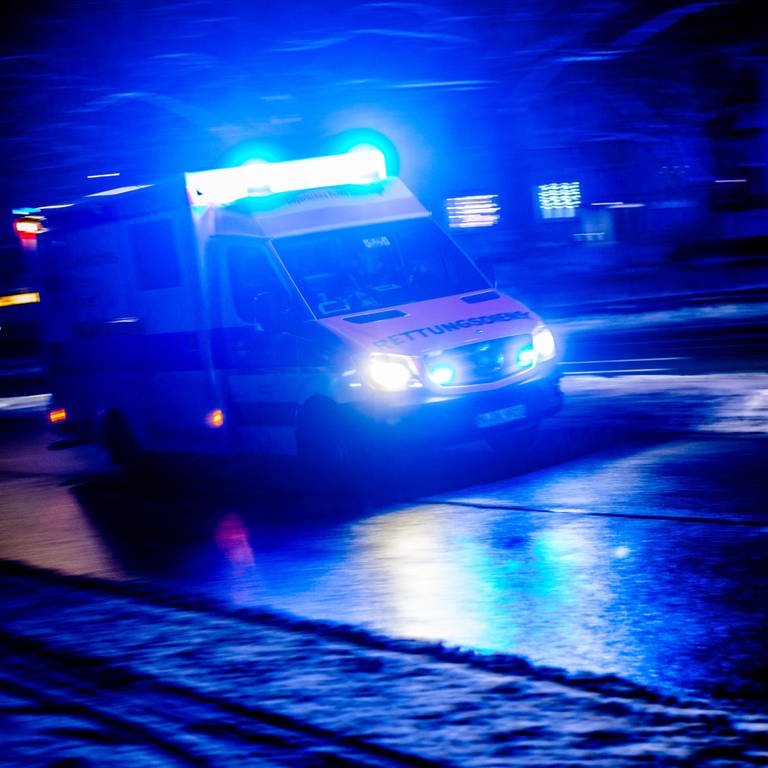 Ein Rettungswagen fährt nachts mit eingeschaltetem Blaulicht durch eine Straße. (Foto: dpa Bildfunk, picture alliance / dpa | Nicolas Armer)