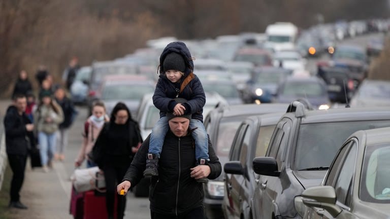 Ukrainische Flüchtlinge gehen mit ihrem Gepäck an Fahrzeugen entlang, die am Grenzübergang stehen.
