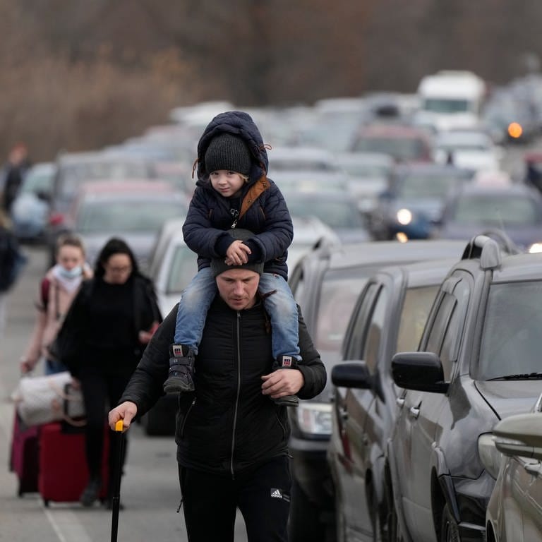Ukrainische Flüchtlinge gehen mit ihrem Gepäck an Fahrzeugen entlang, die am Grenzübergang stehen.
