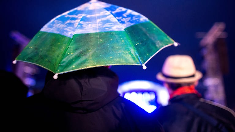 Auf einer Open-Air Veranstaltung regnet es, deshlab haben Menschen einen Schirm. (Foto: dpa Bildfunk, Hauke-Christian Dittrich)