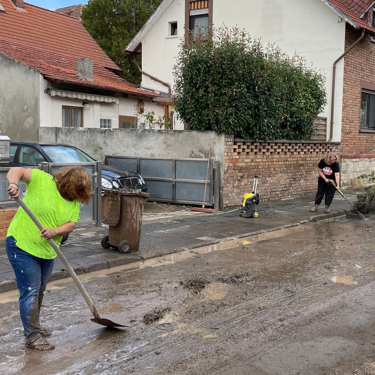 In Worms-Pfeddersheim kratzen und spülen Frauen den Schlamm von den Straßen. Regen und Hagel hatten in und um Worms am Dienstagabend schwere Schäden angerichtet.