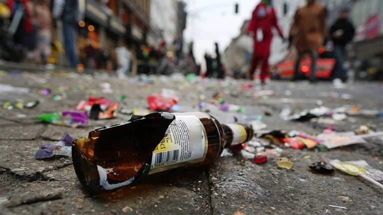 Eine zerbrochene Bierflasche aus Glas und Kofetti liegen auf einer Straße. 
