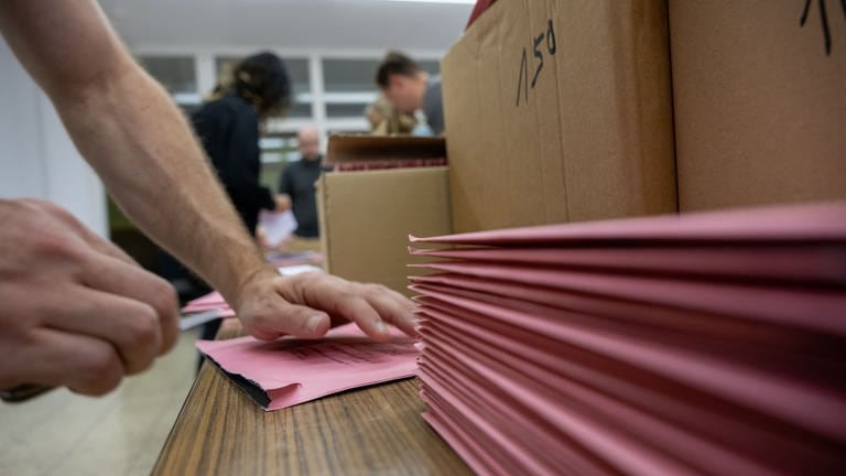 Wahlhelfer öffnen in einem Wahllokal Briewahlunterlagen. 