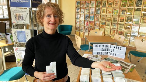 Annette Nagel betreut das Projekt Saatgut in der Wormser Stadtbibliothek. Auf dem Bild steht sie vor der Samenbox und hält trockene Erbsen in der Hand, die eingepflanzt werden können. (Foto: SWR, K. Pezold)