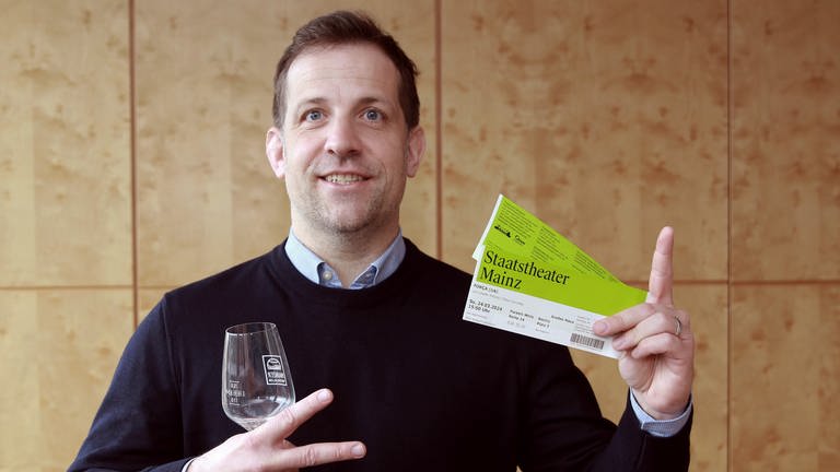 Nino Haase hält eine Karte fürs Theater und ein Weinglas in der Hand