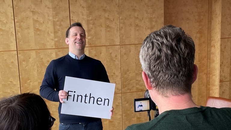 Nino Haase gibt in Mainz ein Interview und hält ein Schild mit der Aufschrift "Finthen" in der Hand (Foto: SWR, D.Brusch)